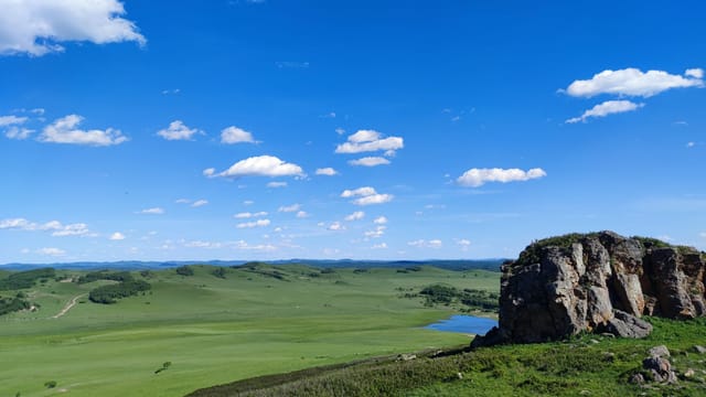A breathtaking view of expansive grasslands under a bright blue sky, featuring a rugged rocky outcrop.