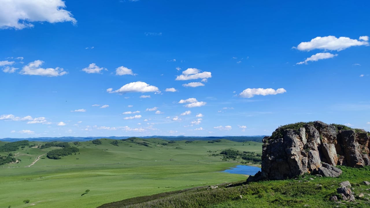 A breathtaking view of expansive grasslands under a bright blue sky, featuring a rugged rocky outcrop.