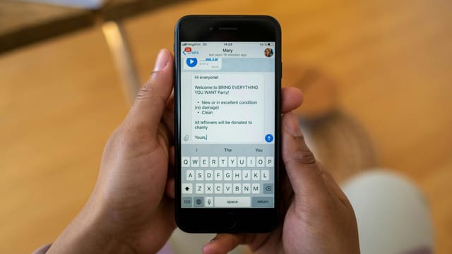 Person holding a smartphone displaying a text message about a party event indoors.