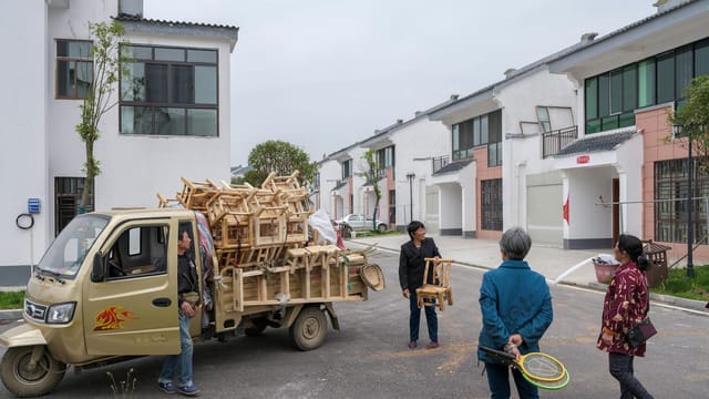 A truck loaded with wooden chairs is being unloaded in an urban area.