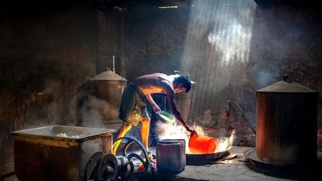 A man engaged in traditional industrial work with lighting beams highlighting his activity amidst equipment.