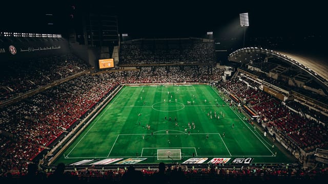 High-angle view of a vibrant football match with enthusiastic fans in a large stadium at night.