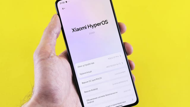 Close-up of a smartphone displaying Xiaomi HyperOS interface, held by a hand against a bright yellow background.