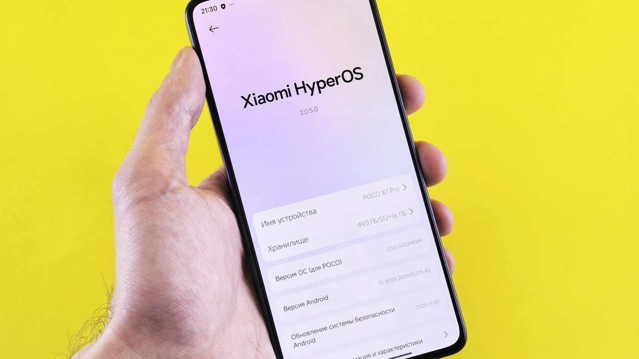 Close-up of a smartphone displaying Xiaomi HyperOS interface, held by a hand against a bright yellow background.