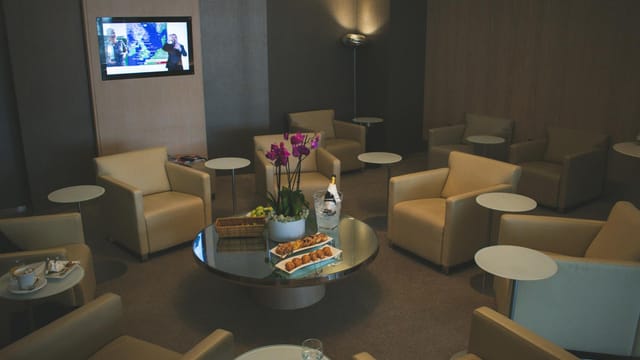 Elegant airport lounge with beige leather seats and orchid decor, offering comfort and luxury food service.