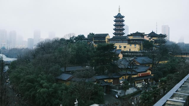 Dramatic view of an ancient pagoda in Nanjing, China, with urban skyscrapers in the misty background.
