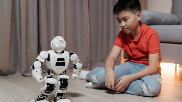 An asian boy sitting on the floor, interacting with a white robot, showcasing innovation and technology.