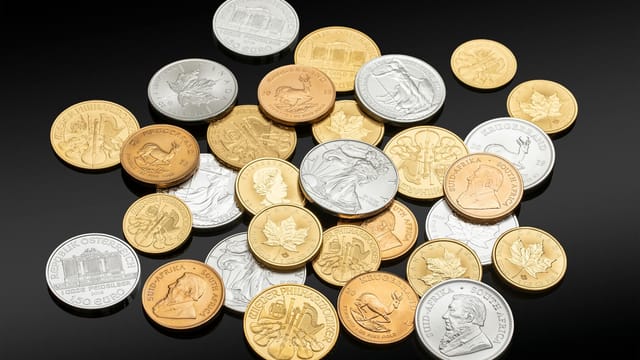 Close-up of assorted coins in silver, gold, and copper on a black background, showing various currencies and denominations.