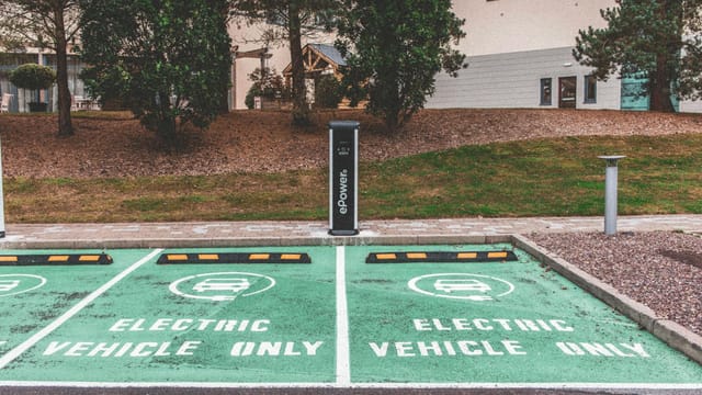 Green electric vehicle parking with charging station in urban environment.