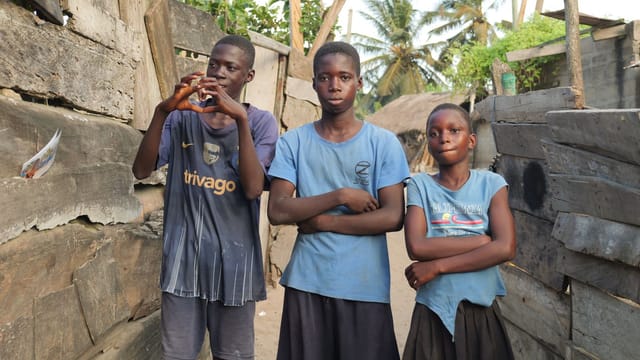 Three boys standing together in an alley of an African village, showing camaraderie and local life.