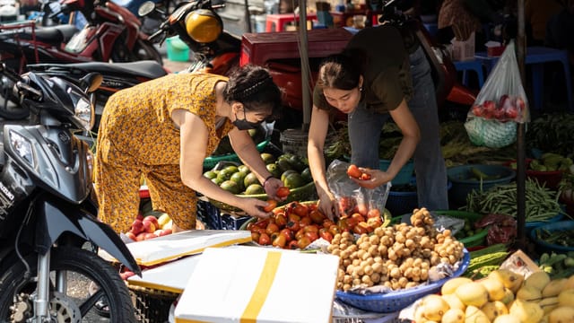 Two women selecting fresh produce at a bustling outdoor market.
