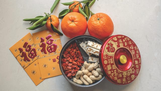 A vibrant flatlay showcasing traditional Chinese New Year items including oranges, hongbao, and festive snacks.