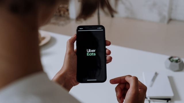 Person holding a smartphone using Uber Eats. Indoor setting with a clear view of the app interface.