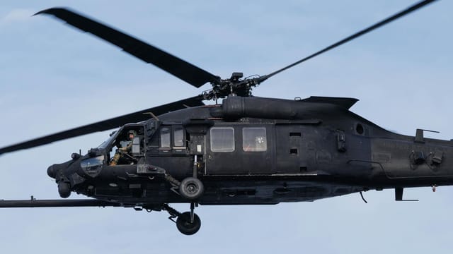A black military helicopter flying in clear blue skies, showcasing precision aviation.