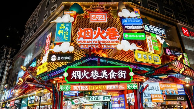 Colorful neon signs illuminate Wuhan's bustling snack street at night.