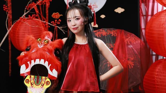 Woman in traditional attire holding a dragon mask at Lunar New Year celebration, vibrant red decorations.