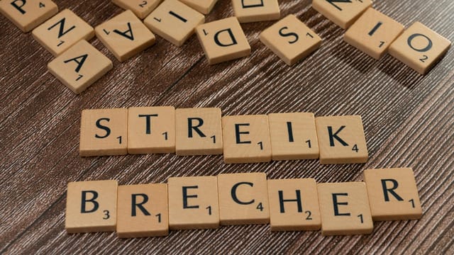 Wooden Scrabble tiles spelling 'Streik Brecher' on a wooden surface.