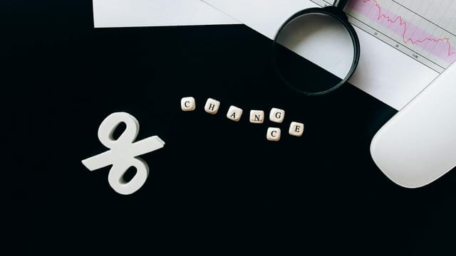 Magnifying glass on financial documents with a percentage sign, symbolizing economic change.