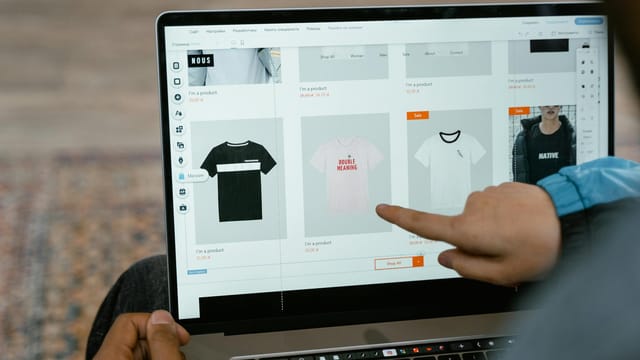 A person points to t-shirt options in an online store on a laptop screen.