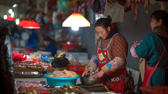 Busy market in Guilin, Guangxi, China with vendors preparing fresh foods under warm lights.