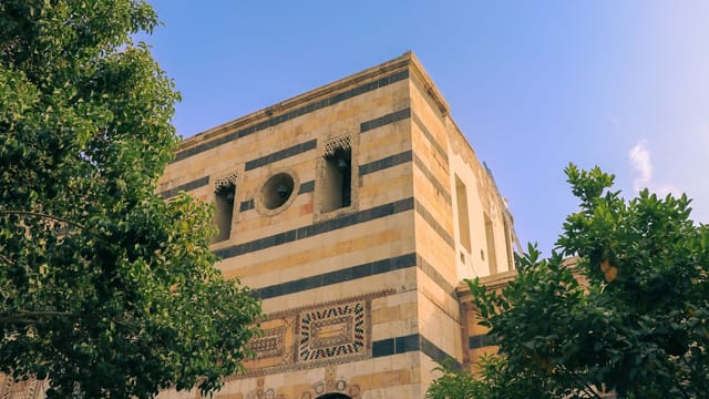 A beautiful historic building with a striped facade in Damascus, Syria, surrounded by lush greenery.