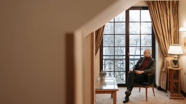 A man relaxes in a cozy living room with large windows and elegant decor.