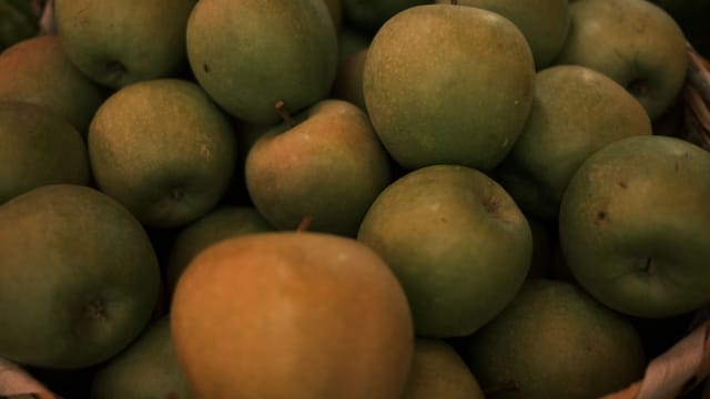 Close-up of fresh green apples piled in a basket, showcasing their lush texture.