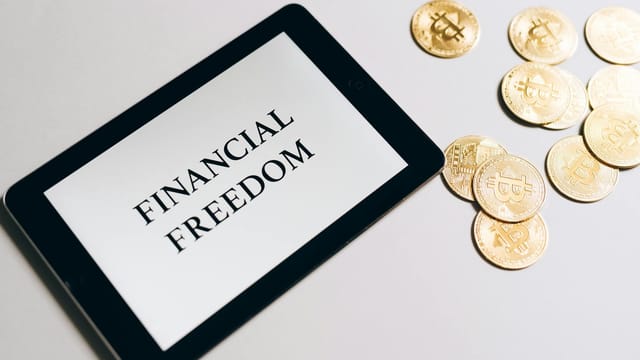 Tablet showing 'Financial Freedom' with gold bitcoins nearby, symbolizing cryptocurrency investment.