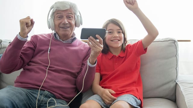 Smiling grandfather and granddaughter enjoying media on a smartphone at home.