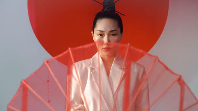 Stylish portrait of an Asian woman in a white blazer with a traditional hair bun and red umbrella.