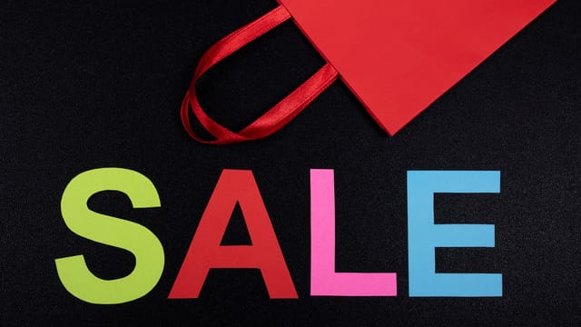 Vibrant text 'SALE' next to a red paper bag on a black background.