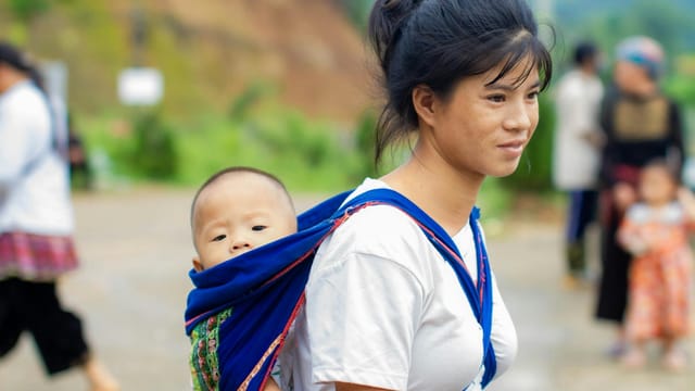 A mother carrying her baby in a colorful sling outdoors, evoking warmth and culture.