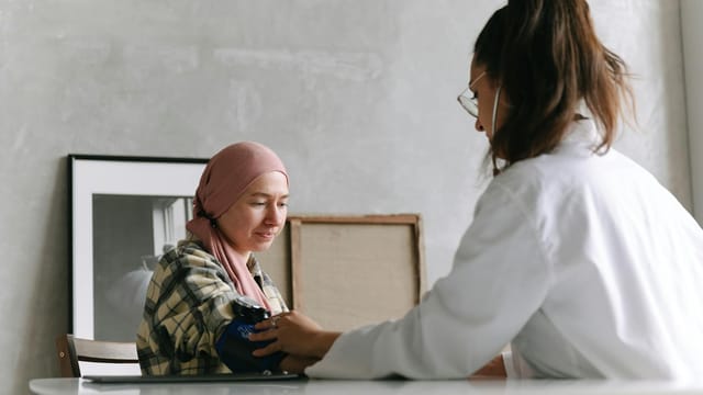 Doctor checks blood pressure of a patient wearing a headscarf indoors, focused on healthcare.
