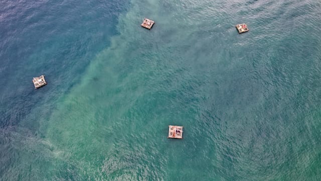 Aerial view showcasing floating rafts in the emerald waters of Pelabuhan Ratu, Indonesia.