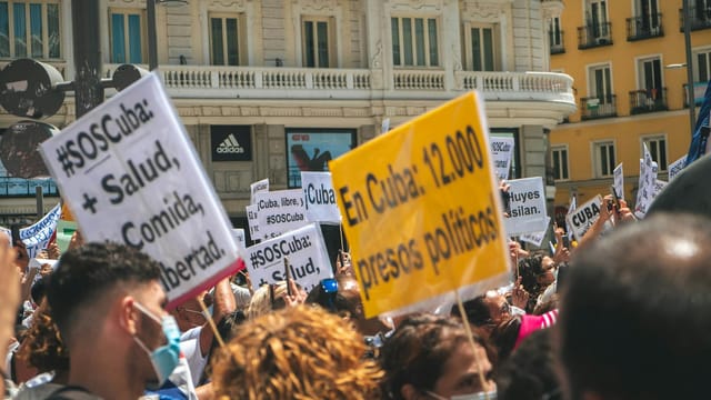 Crowd of activists in Cuba rallying for political reform, holding placards and wearing face masks.