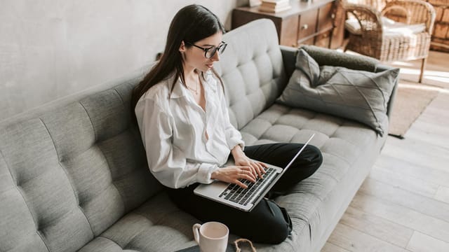 Woman in a cozy home setting working on a laptop for remote work and relaxation.