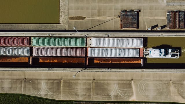 Drone view of barge carrying many aged ribbed metal containers on city canal in daytime