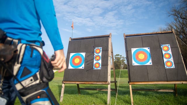 An archer prepares for target practice in an open field under a clear sky.