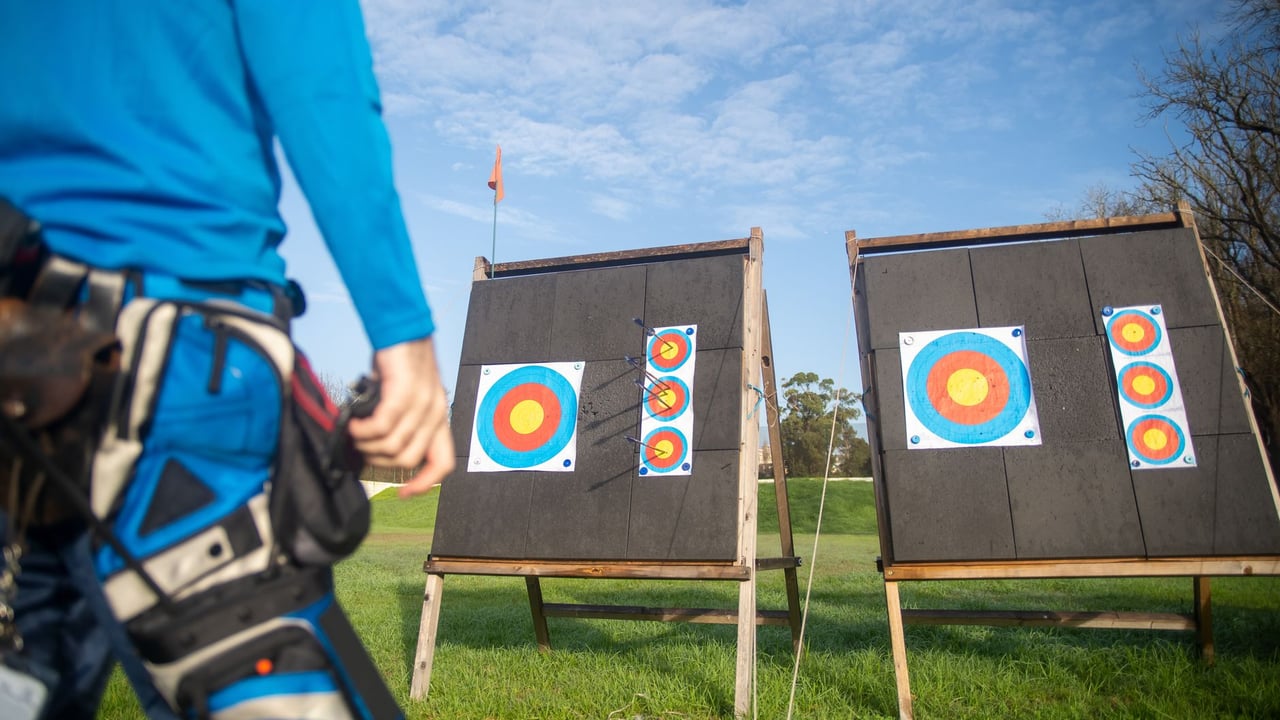 An archer prepares for target practice in an open field under a clear sky.