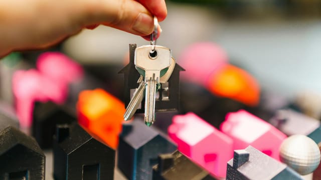 Colorful miniature houses and a hand holding keys representing real estate decisions.