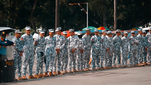 A group of soldiers in camouflage uniforms standing in line outdoors during the day.
