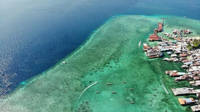 Boats floating on rippling endless sea near island with various residential houses in tropical country on summer day in nature
