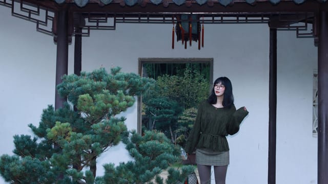 Woman standing in a traditional Chinese garden in Nanjing, China, wearing fashionable clothing.