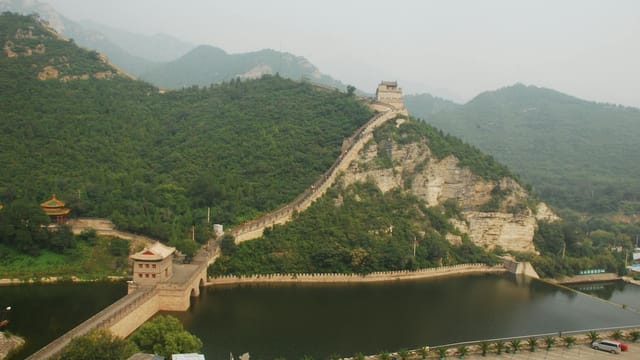 Scenic view of the Great Wall of China traversing lush green mountains and a tranquil river.