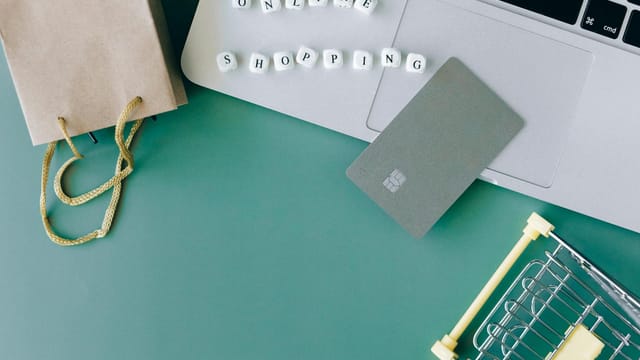 Flat lay of online shopping essentials with laptop, card, and shopping cart.