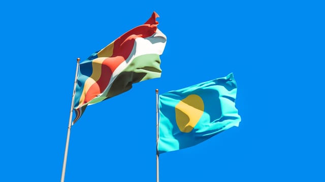 Two national flags waving in the wind against a clear blue sky, representing Seychelles and Palau.