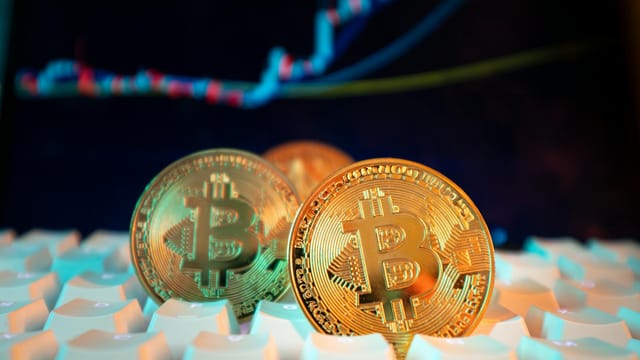 Golden Bitcoin coins on a keyboard with a financial chart in the background, representing digital currency and market trends.