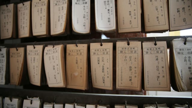 A collection of vintage library catalog cards hanging on wooden shelves, showcasing traditional Japanese text.