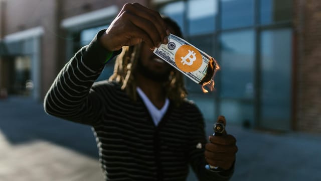 Man holding a burning dollar bill with Bitcoin symbol. Conceptual image of cryptocurrency impact.