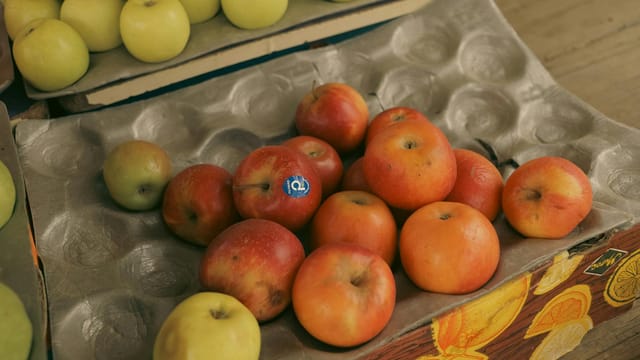 A variety of fresh red and green apples displayed in cardboard trays at an outdoor fruit market.